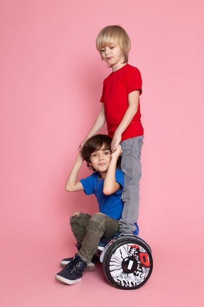 Una vista frontale due ragazzi in magliette rosse e blu a cavallo segway sullo spazio rosa