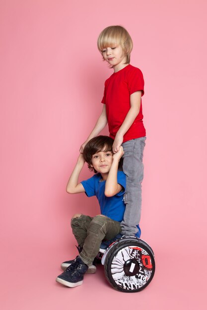 A front view two boys in red and blue t-shirts riding segway on the pink space