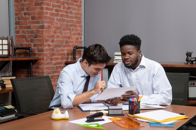 Вид спереди двух бизнесменов, обсуждающих материалы офиса проекта на столе