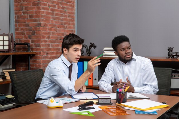 Front view two businessmen sitting at desk and looking at something in office