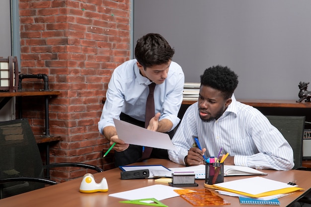 Free photo front view two busy businessmen in formal wear one of them showing paper to another one in office