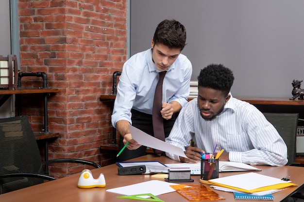 Front view two busy businessmen in formal wear one of them showing paper to another one