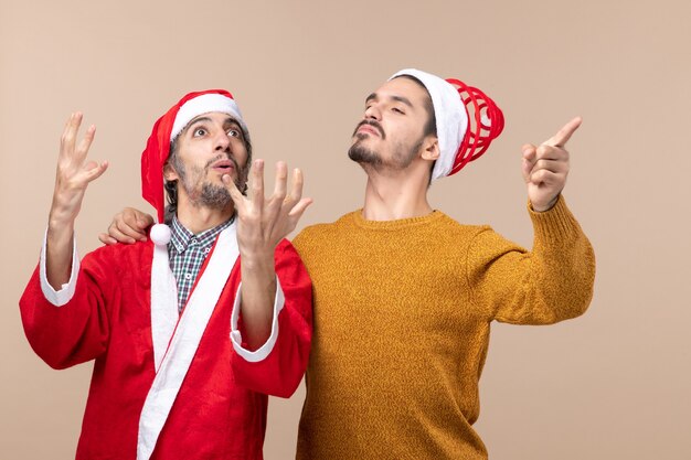 Front view two confident men with santa hats standing on beige isolated background