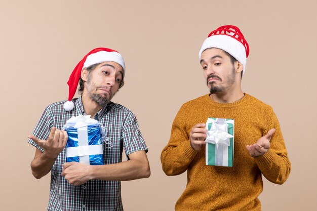 Front view two confused guys holding christmas presents on beige isolated background