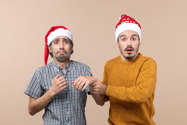 Front view two depressed guys with santa hats on beige isolated background