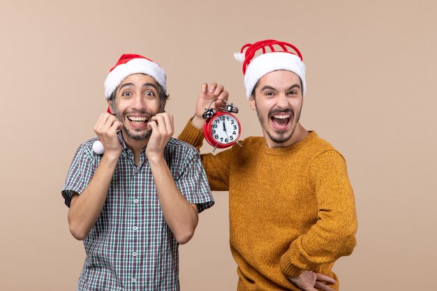 Front view two elated men one holding an alarm clock standing on beige isolated background