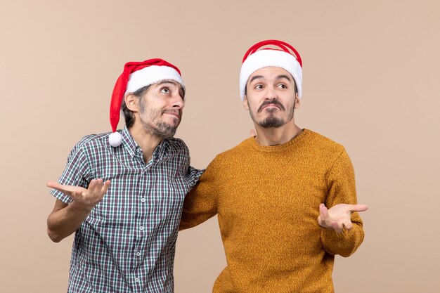 Front view two emotional careless guys with santa hats on beige isolated background