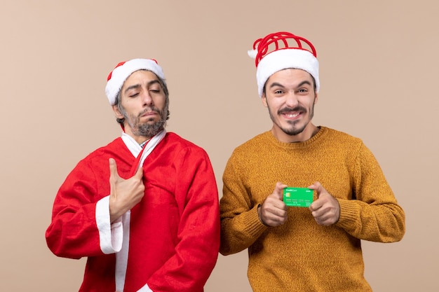 Front view two friends one with santa coat and the other with credit on beige isolated background