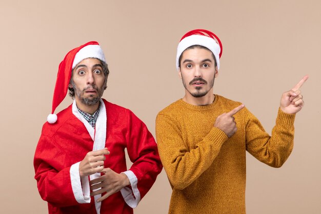 혼란스러운 산타 모자와 베이지 색 격리 된 배경에 다른 표시 방향으로 전면보기 두 친구
