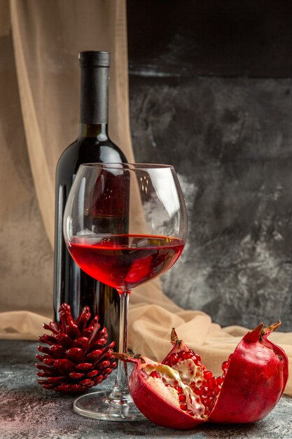 Front view of two glasses and bottle with delicious dry red wine and open pomegranate conifer cone on ice background