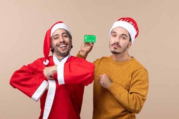 산타 코트 미소와 베이지 색 격리 된 배경에 카메라를보고 신용 카드로 다른 하나는 전면보기 두 사람