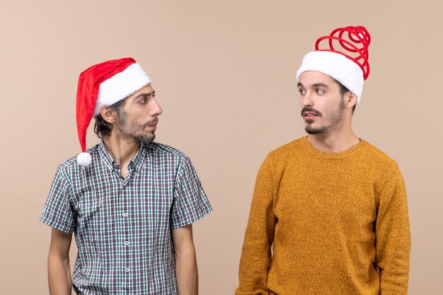 Front view two guys with santa hats looking at each other on beige isolated background