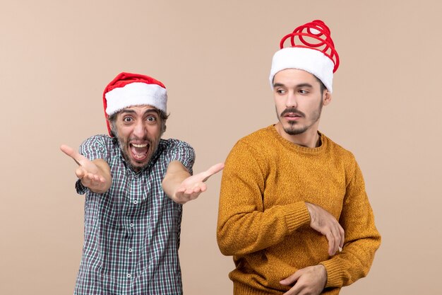 Front view two guys with santa hats one shouting and the other confusing on beige isolated background