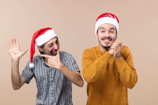 그의 손을 보여주는 산타 모자와 전면보기 두 사람이 다른 닫힌 눈 베이지 색 격리 된 배경으로 소원