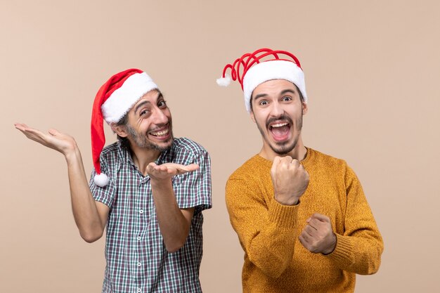 베이지 색 격리 된 배경에 열린 손과 다른 펀치와 함께 서있는 산타 모자와 함께 전면보기 두 행복한 사람