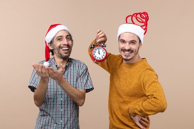 Front view two happy men holding an alarm clock and smiling on beige isolated background