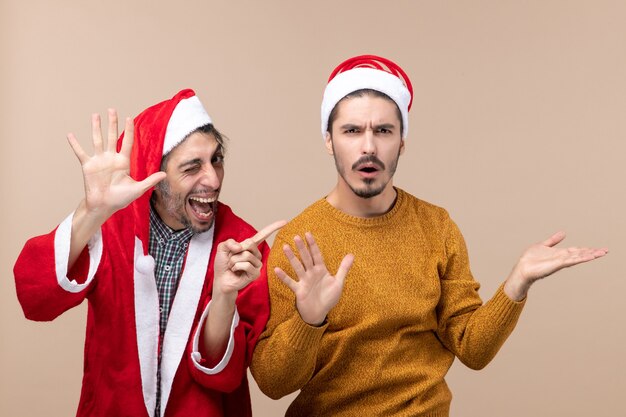 Front view two happy men one with blinked eye and the other serious face on beige isolated background