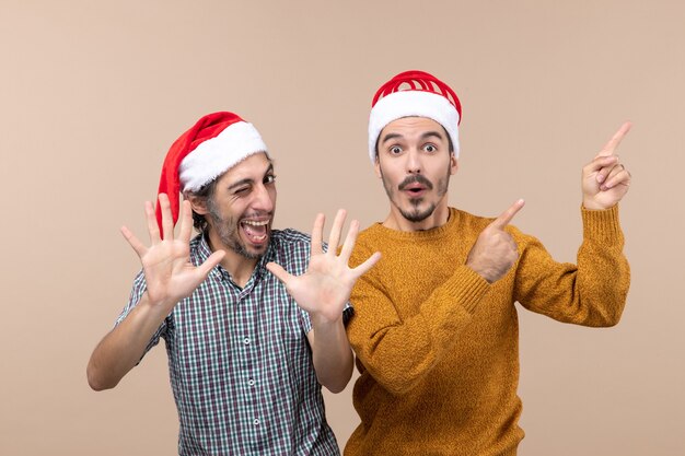 Вид спереди двух счастливых мужчин в шляпах санта-клауса, один показывает что-то, а другой делает пятерку на изолированном фоне