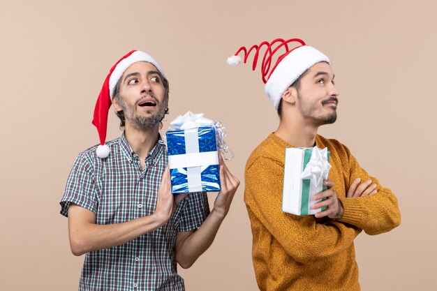 Front view two interested guys wearing santa hats and thinking presents