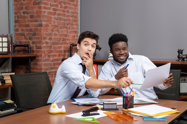 Front view two joyful businessmen satisfying working together one of them pointing at paper