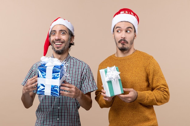Front view two men a happy and confused wearing santa hats on beige isolated background