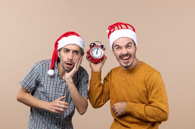 Front view two men one confusing and the other holding an alarm while laughing clock on beige isolated background