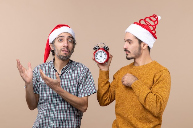 Front view two men one holding an alarm clock and the other confusing it on beige isolated background