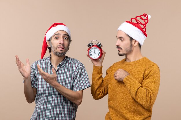 正面図2人の男性、1人は目覚まし時計を持っており、もう1人はベージュの孤立した背景でそれを混乱させています