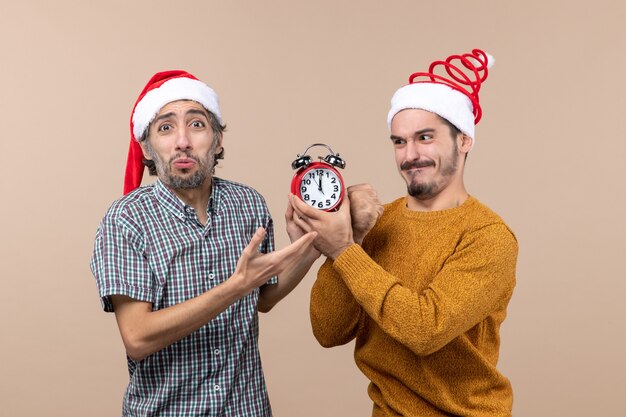 Front view two men one holding an alarm clock and trying punch it on beige isolated background