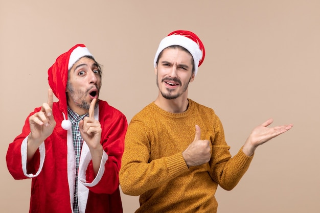 Front view two men one putting finger to his mouth and the other showing something on beige isolated background