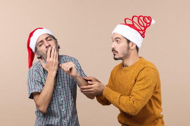 Front view two men a sleepy and a confused one holding the others arm on beige isolated background