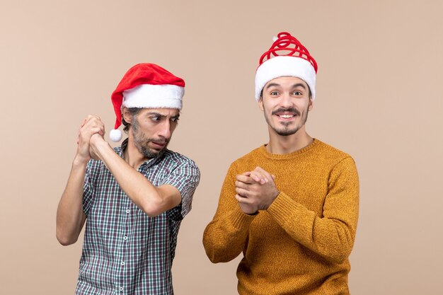 Front view two men with santa hats holding hands together on beige isolated background