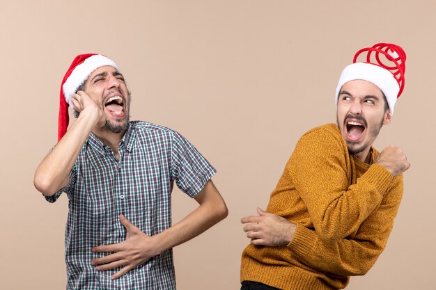 Front view two shouted guys with santa hats on beige isolated background