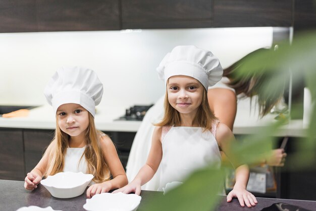 Front view of two siblings standing near kitchen counter wearing chef hat and apron