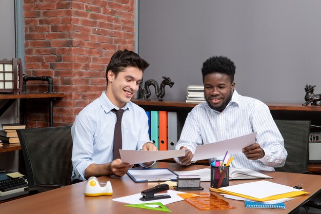 Front view two smiling businessmen sitting at desk working together in office