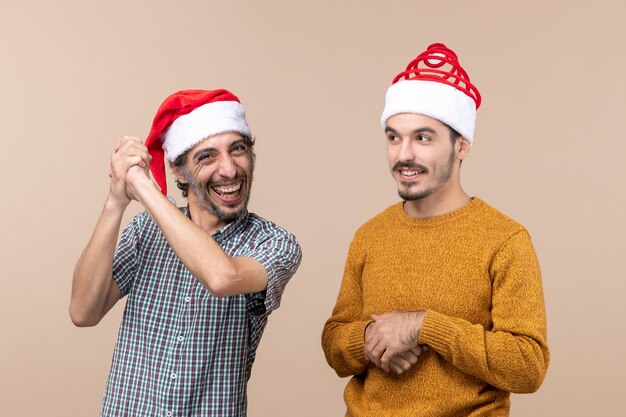 Front view two smiling guys with santa hats on beige isolated background