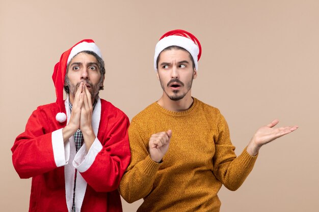 Front view two surprised men one putting hands on his mouth and the other showing something on beige isolated background