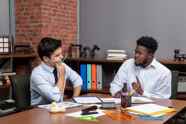 Free photo front view two untiring businessmen sitting at desk and discussing project in office