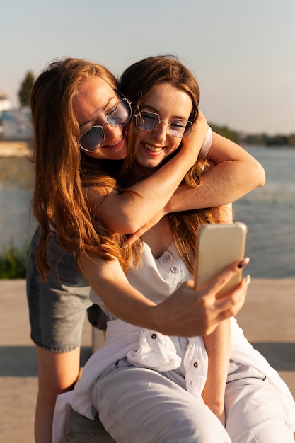 Vista frontale di due donne che prendono un selfie in riva al lago