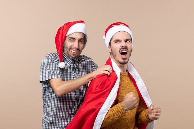 베이지 색 격리 된 배경에 그의 친구 어깨에 산타 코트를 입고 전면보기 두 크리스마스 남자 하나