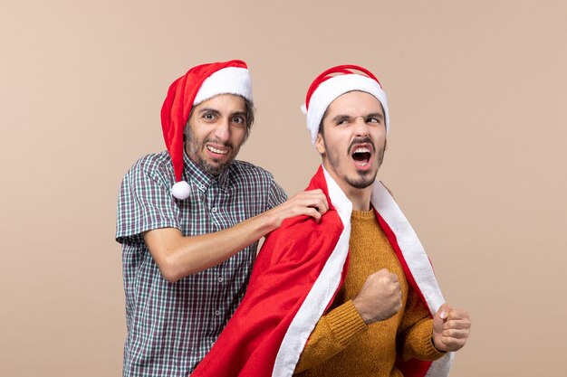 Front view two xmas guys one putting santa coat on his friends shoulder on beige isolated background