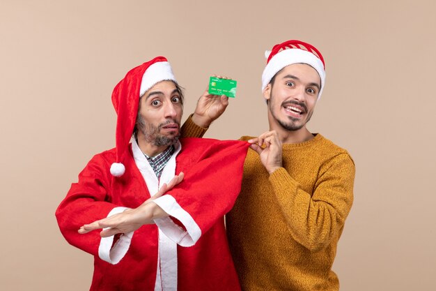 Front view two xmas guys one with santa coat and the other with credit card pulling his friends coat on beige isolated background