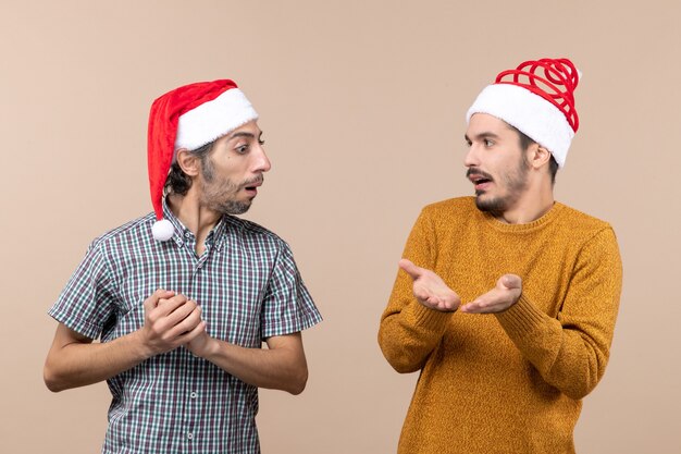 베이지 색 격리 된 배경에 다른 뭔가를 보여주는 산타 모자 하나 전면보기 두 크리스마스 남자