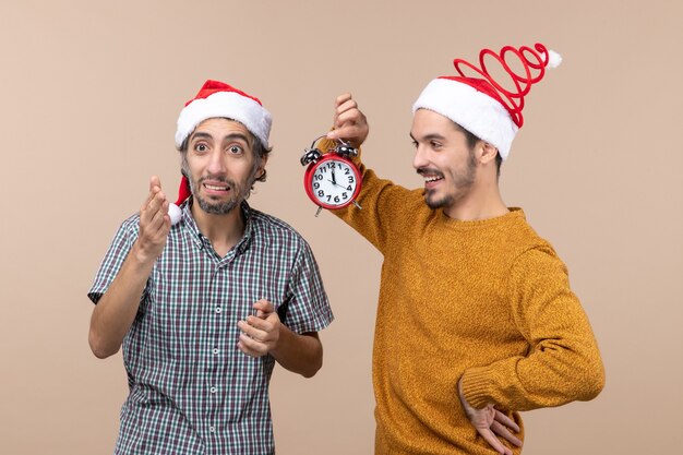 베이지 색 격리 된 배경에 알람 시계를 들고 전면보기 두 크리스마스 남자