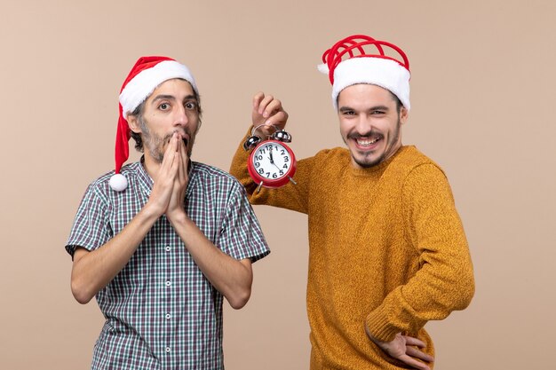 Front view two xmas men a surprised and a happy one holding an alarm clock on beige isolated background