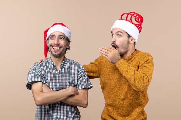 Vista frontale due uomini di natale con cappelli di babbo natale uno che mostra qualcosa all'altro su sfondo beige isolato