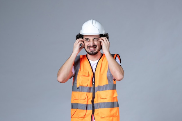 회색 파도 벽에 안전 헬멧과 함께 경고 조끼를 입고 불확실한 불확실한 남성 건축업자의 전면 보기