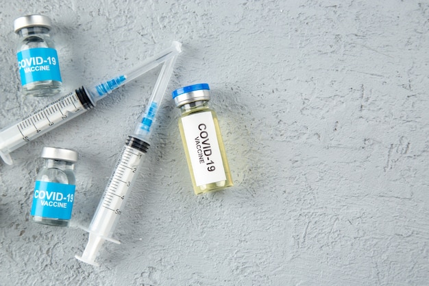 회색 모래 배경의 오른쪽에 있는 다양한 코비드-백신 및 주사기의 전면 보기