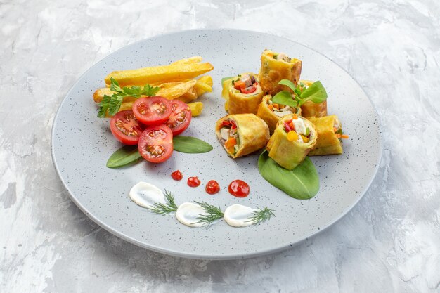 Front view vegetable pate rolls with tomatoes and french fries inside plate on white surface
