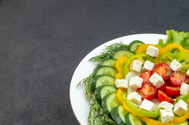正面図の野菜サラダは、暗い背景にスライスしたキュウリ、トマト、コショウ、チーズで構成されています